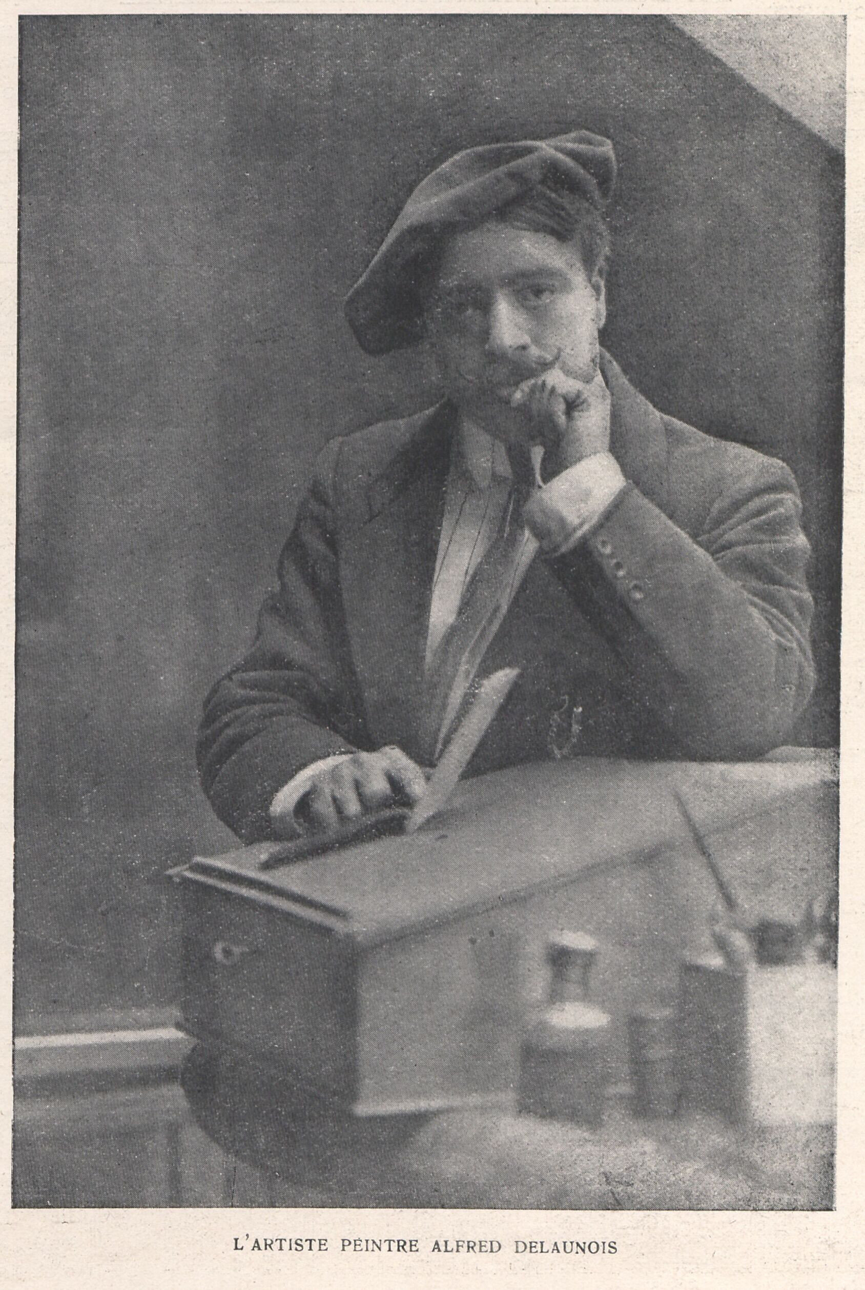 Black and white photograph of the painter Alfred-Napoléon Delaunois posing in his studio, with painting materials nearby.