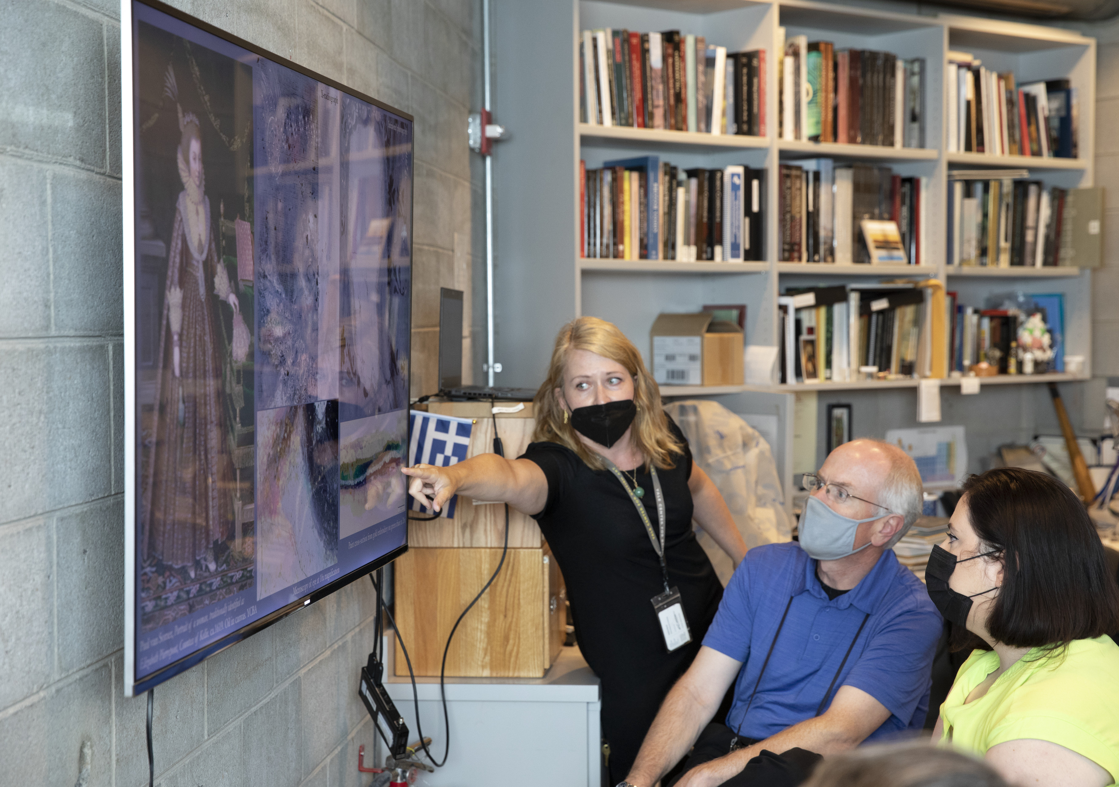 YCBA office interior showing seated participants listening to a STITAH leader pointing to a close-up photograph on a flat screen TV.