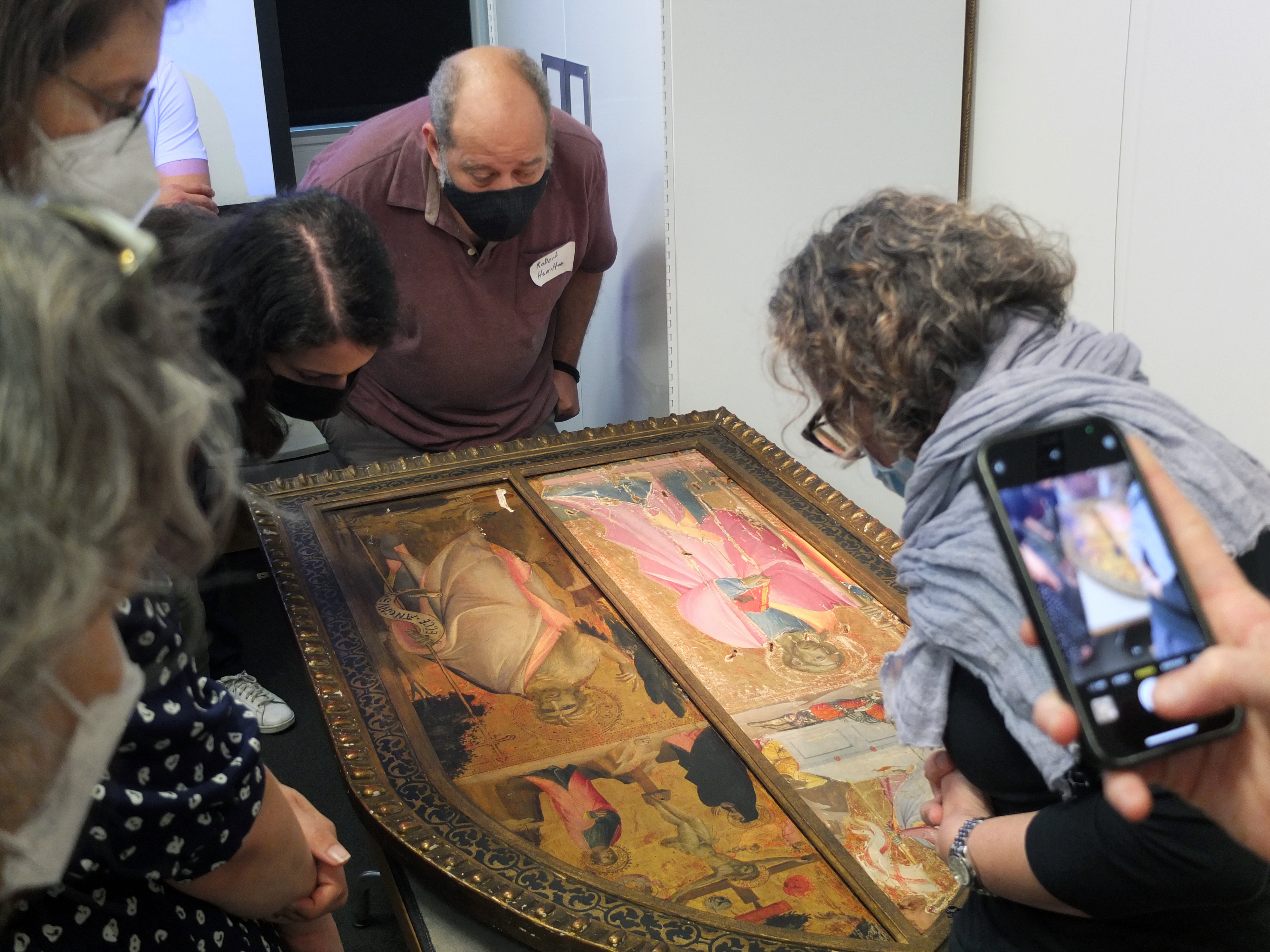 Group of STITAH participants and leaders looking down at a Medieval painting enclosed inside a golden Gothic-arched frame in YUAG.