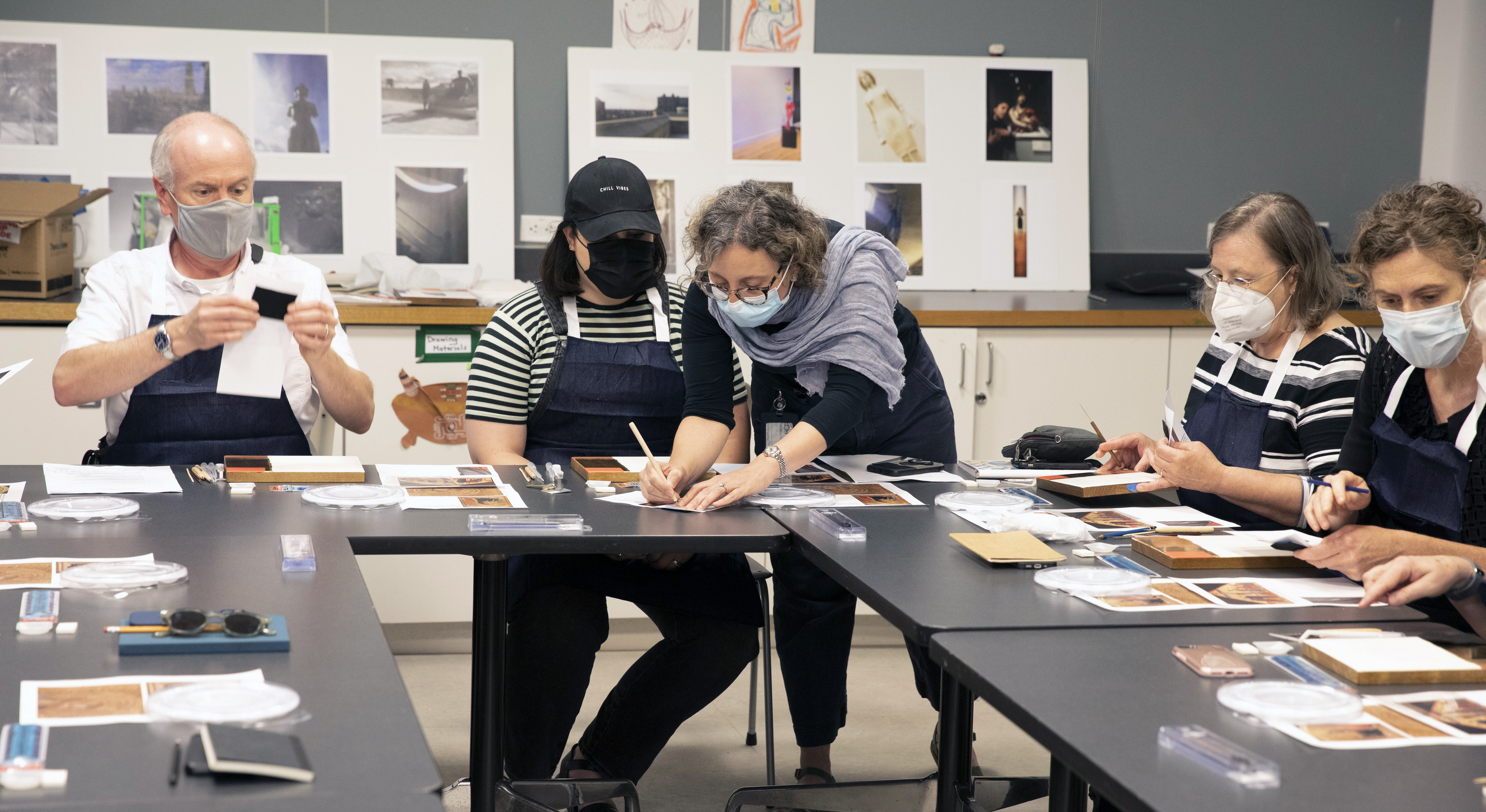 YUAG classroom view of one standing STITAH leader assisting seated participants at tables with techniques such as cartoon drawing transfers.