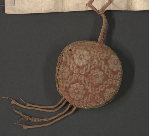 Front of the red-pinkish silk seal bag decorated with white flower medallions.