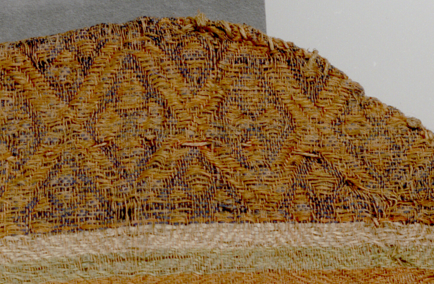 Close-up detail of a band with orange lozenge medallions on a dark blue background, showing an undyed thread sewn across the fabric.